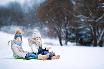 Fototapeta na wymiar Little adorable girls enjoy a sleigh ride. Child sledding. Children play outdoors in snow. Family vacation on Christmas eve outdoors