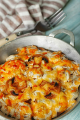 Roasted mushrooms, chicken and cheese gratin in pan, on wooden background