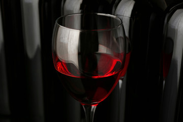 Red wine glass against bottles in a row on black background, close up