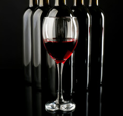 Red wine glass against bottles in a row on black background, close up