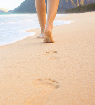 Beach travel. Woman walking on sand beach leaving footprint in the sand.
