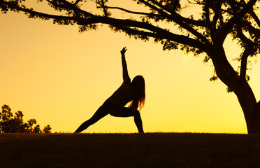 Young girl doing yoga under a tree. 