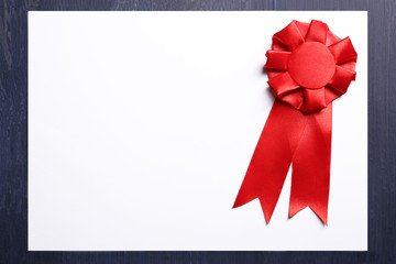 Award ribbon on white paper sheet, on wooden background