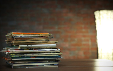 Pile of old books on wooden table against brick wall, close up