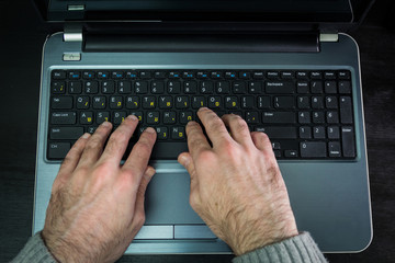Man typing on a keyboard with letters in Hebrew and English - Laptop keyboard - Top View - Dark atmosphere