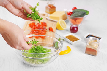 Female hands adding lettuce leaves into bowl with salad, close-up