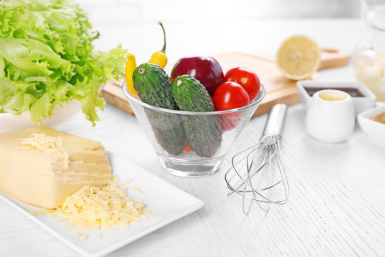 Kitchen utensils and ingredients for salad on table, on light background