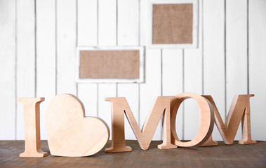 Fototapeta na wymiar I love mom inscription of wooden letters with heart and flowers on white wall background