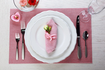 Table setting with dishes, cutlery, napkin and candles on pink background
