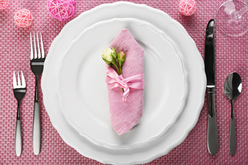 Table setting with dishes, cutlery and napkin on pink background