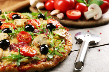 Delicious tasty pizza with cutter and ingredients on wooden table