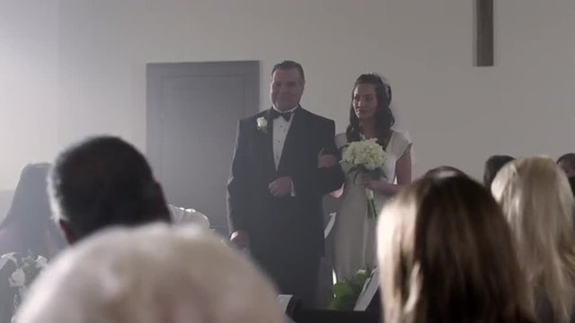 Uncertain looking bride being escorted down the aisle.