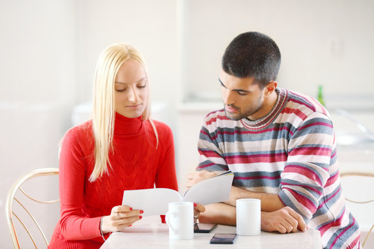 Young couple reading magazine together and drinking coffee at home