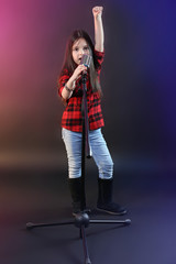 Beautiful little girl with microphone on dark purple background