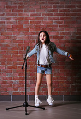 Beautiful little girl with microphone on brick wall background