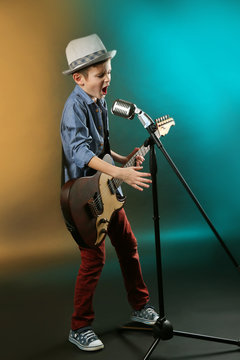 Little boy playing guitar and singing with microphone on a dark lighted background