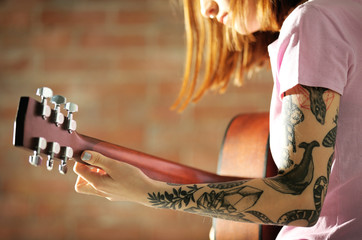 Attractive woman with tattoo playing guitar on brick background