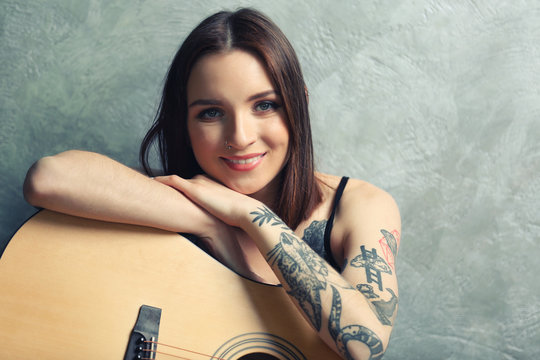 Woman with tattoo and guitar sitting on grey background