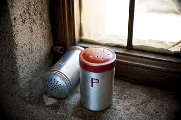 Salt and pepper shaker with red top on windowsill and spilled salt
