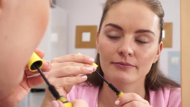 Woman applying black eye mascara to her eyelashes 4K
