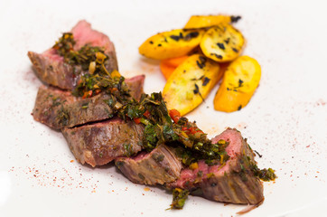 Delicious medallions of tenderloin steak placed upon white dinner plate with some vegetables next to it, elegant presentation