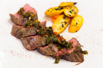 Delicious medallions of tenderloin steak placed upon white dinner plate with some vegetables next to it, elegant presentation