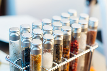 Tubes of spices placed inside metal rack and some plates blurry in background