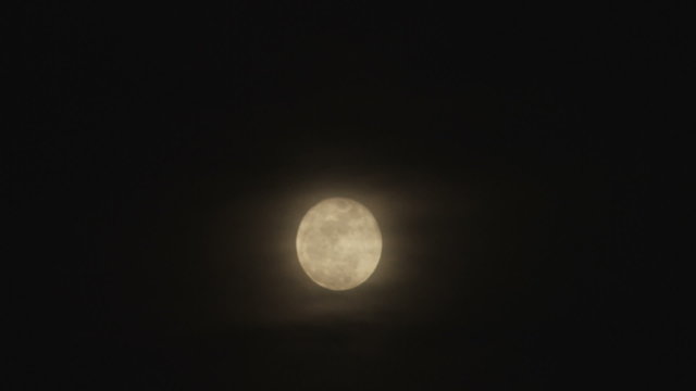 Wide shot of a full moon and clouds passing in front.