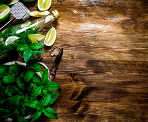 The ingredients for the cocktail - limes, rum, mint leaves, ice cubes on wooden table. Free space for text.