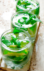 Three cocktail glasses with ice cubes, lime, mint leaves and rum . On the old background.