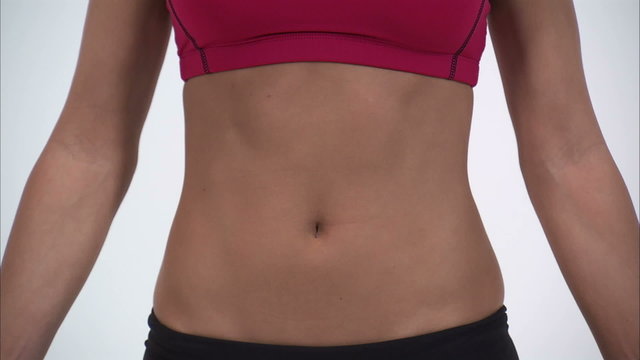 Close up of a woman's abdomen as she puts her hands on her hips.