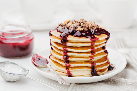 Stack of american pancakes or fritters with blackcurrant jam in plate on white table, delicious dessert for breakfast