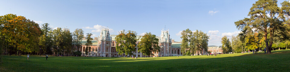 Fototapeta na wymiar Панорама газона в окружении деревьев перед дворцом в парке Москвы. Осень. Россия.