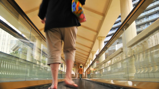 Sped up people on a moving walkway proceeding to a hotel.