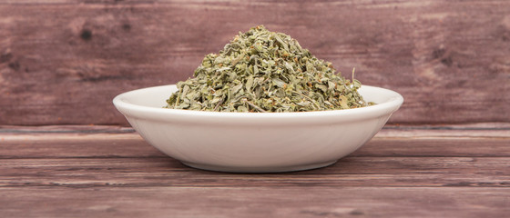 Marjoram herbs in white bowl over wooden background