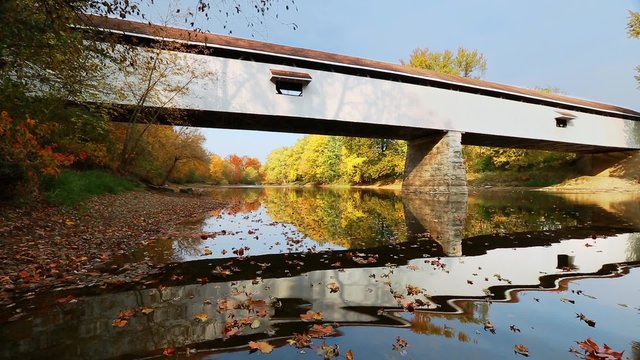Loop features Potter's Covered Bridge, built in 1870, reflected in the waters of Indiana's White River flowing with colorful autumn leaves floating on the surface.
