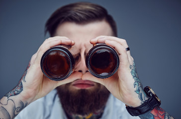 Bearded hipster man holding beer bottles like binocular.