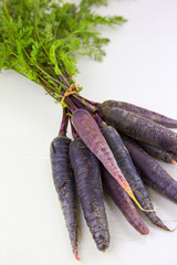 Bunch of heirloom purple carrots, over white and wooden backgrou