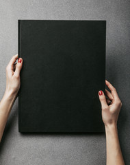 Female hands holding big black book. Vertical