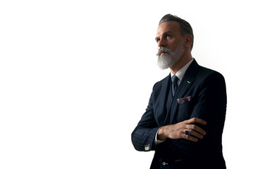 Portrait of bearded gentleman wearing trendy suit and stands against the empty white wall....