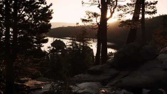 Dark shot of sun peaking through trees over water and&Acirc;&nbsp;stream near Lake Tahoe, California.