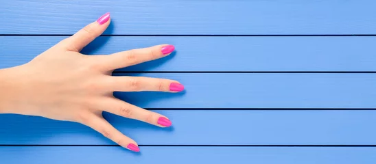 Tuinposter Female hand with pink nails on blue wooden background © Leszek Czerwonka