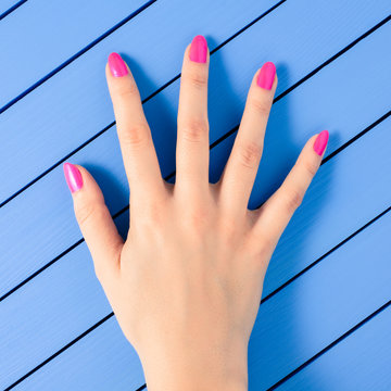 Female hand with pink nails on blue wooden background