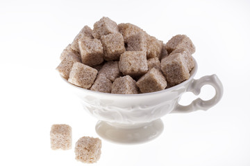 some cane sugar cubes in a small cup on white background