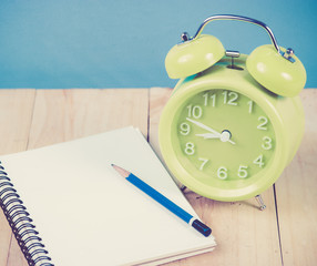 Green alarm clock and Notebook Paper with Text Space on wood,blu