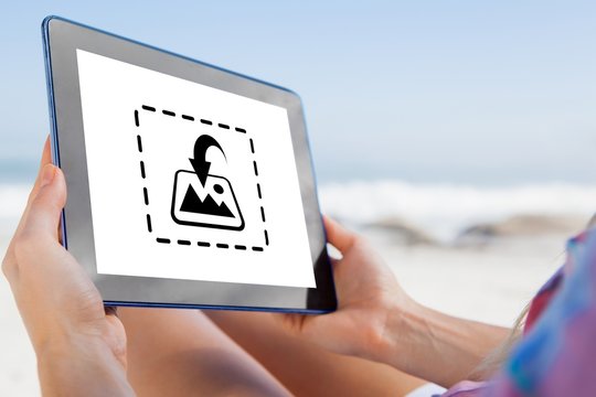 Woman sitting on beach in deck chair using tablet