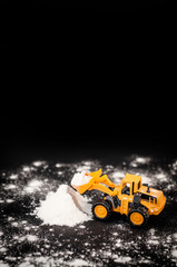 Toy tractor clears snow pile/Photo: yellow toy tractor, hill of artificial snow on a black background. Local focus