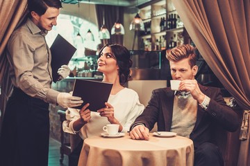 Waiter taking order from stylish wealthy couple in restaurant.