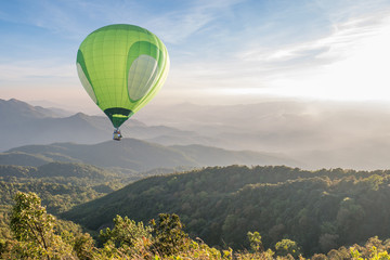 Naklejka premium Green hot air balloon over high mountain landscape at sunset
