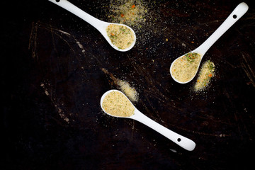 Salt with spices on a spoon, black background, top view.
